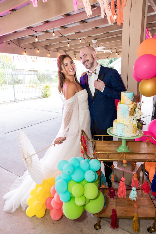 A groom and bride posing with their wedding cake